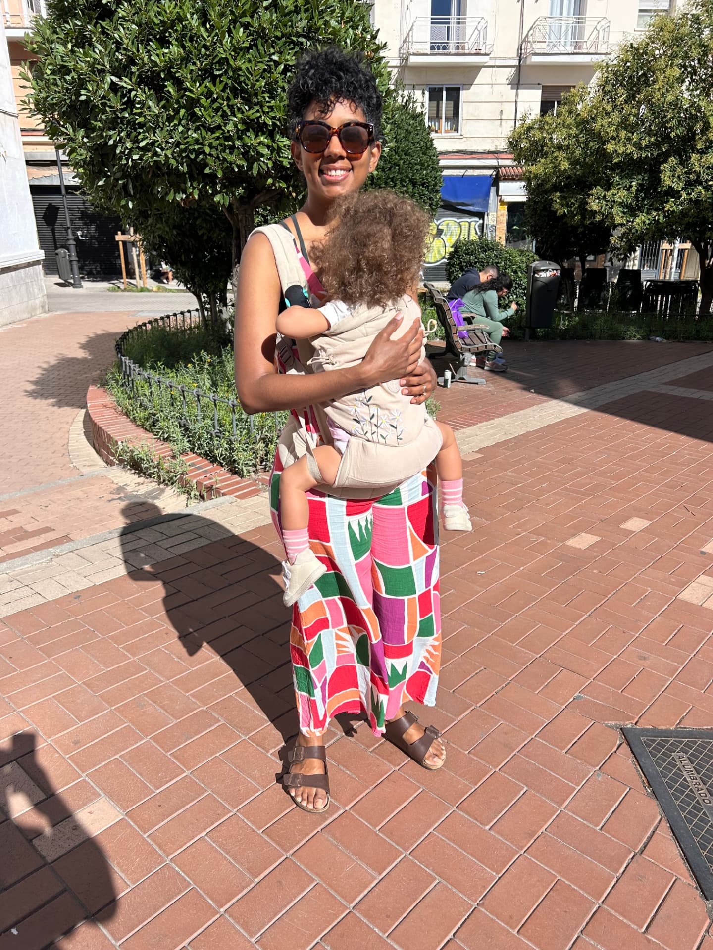 Telma in a colourful dress holding her child in a sunny plaza
